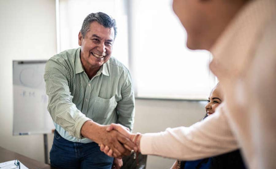 A senior man smiling while shaking hands in a corporate setting.